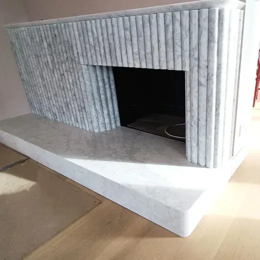 Gray striped miniature fireplace with a black opening and white base on a wooden floor