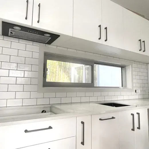 Modern white kitchen with subway tile backsplash, black hardware, and a long window above the sink