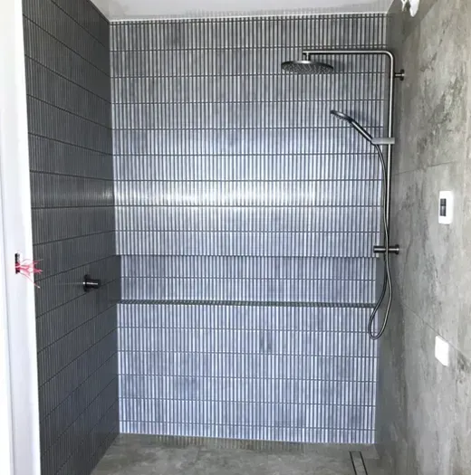 Modern gray tiled walk-in shower with wall-mounted fixtures and handheld showerhead