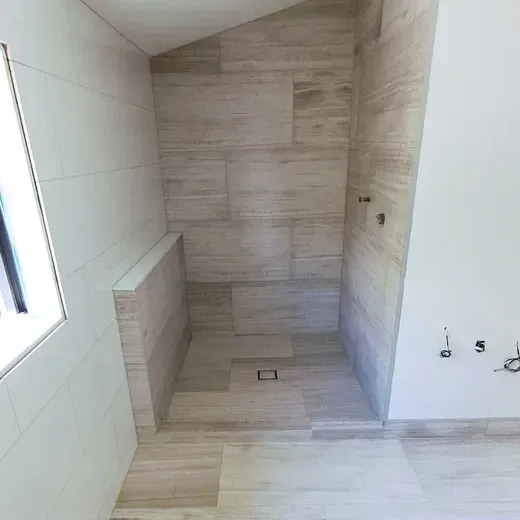 Empty tiled shower alcove with light beige walls, floor drain, and a small window on the left.