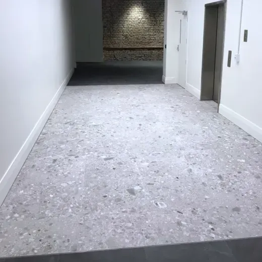 Empty gray hallway with white walls, a doorway, and a dark alcove at the far end.