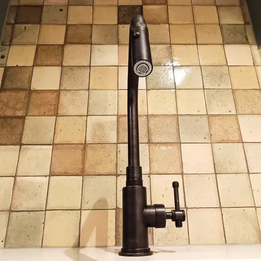Black sink faucet against beige tiled floor background