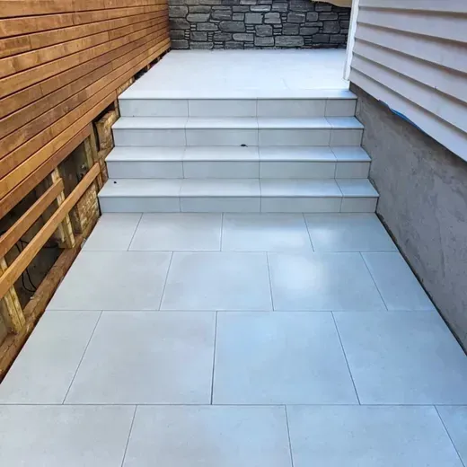 White tiled patio walkway with steps leading up between a wood fence and a house wall
