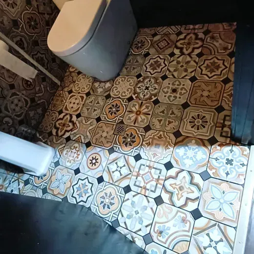 Patterned bathroom floor with two trash bins and a bright patch of sunlight