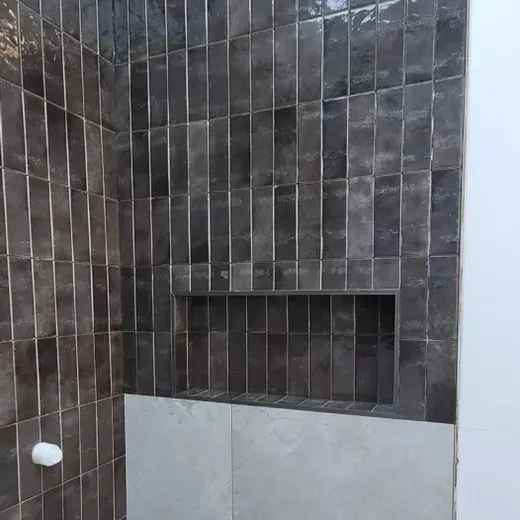 Dark tiled bathroom wall with a recessed shelf above a white tub or sink edge