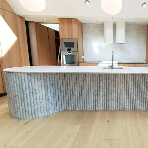 Modern kitchen with curved ribbed island, wooden cabinetry, white countertop, and stainless appliances