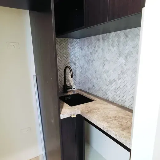 Compact kitchen corner with black sink, dark cabinetry, and beige countertop beneath a gray tiled backsplash