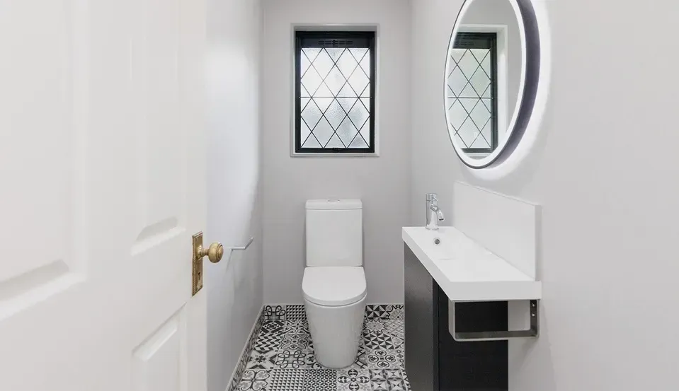 Small modern bathroom with white toilet, sink, round mirror, and patterned tile floor.