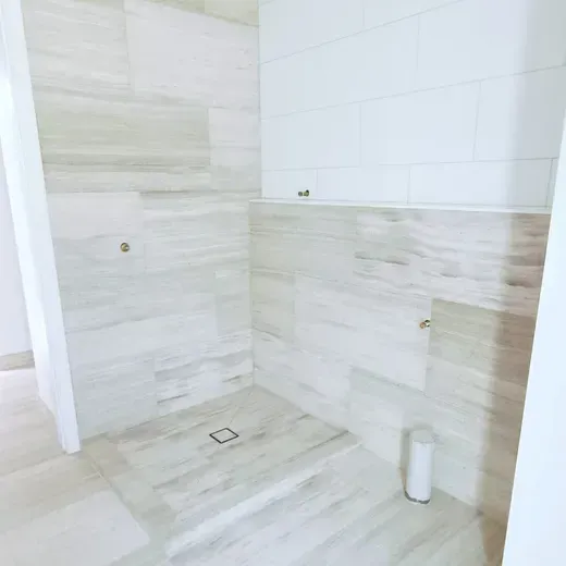 Bright white tiled bathroom shower with a floor drain and wall fixtures