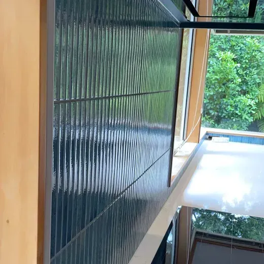 Modern interior with wood paneling, dark ribbed wall, and a large window overlooking green trees