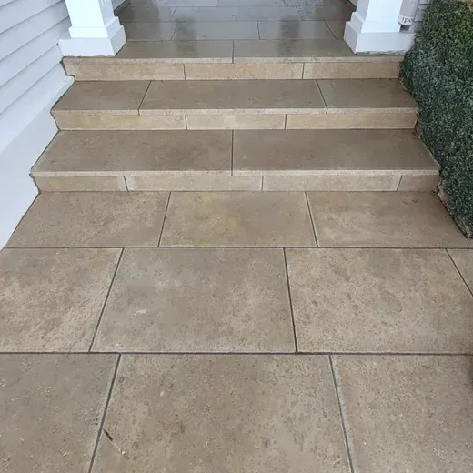 Tan stone steps leading to a porch, flanked by white columns and hedges