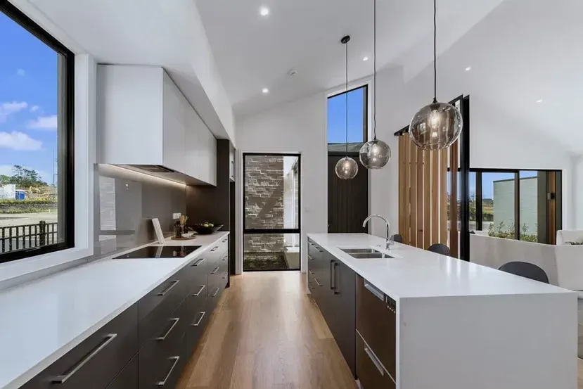 Modern kitchen interior with white island, dark cabinets, wood floor, and large windows