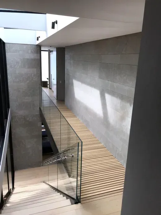 Modern indoor staircase with glass railing and concrete walls lit by sunlight