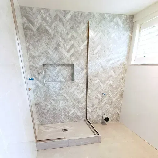Modern bathroom with walk-in shower, gray herringbone tile, and glass partition.