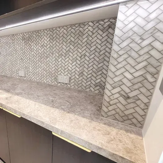 Modern kitchen with beige marble countertop, herringbone tile backsplash, and under-cabinet lighting