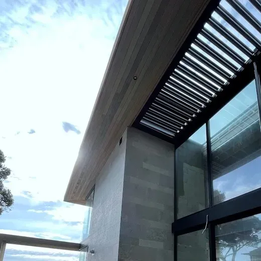 Modern building exterior with a slatted overhang, glass wall, and blue sky overhead