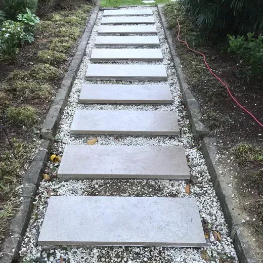 Concrete stepping-stone path ascending through a narrow garden, bordered by gravel and greenery