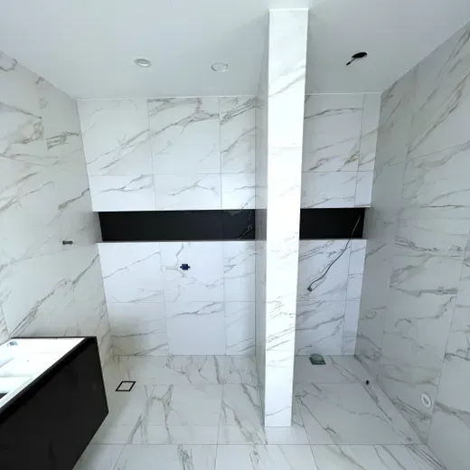 Empty tiled shower with white marble-look walls, black accent band, and central glass partition.