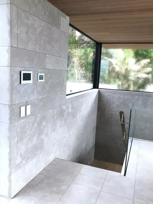 Modern stairwell with gray tiled walls, glass railing, and large windows overlooking greenery