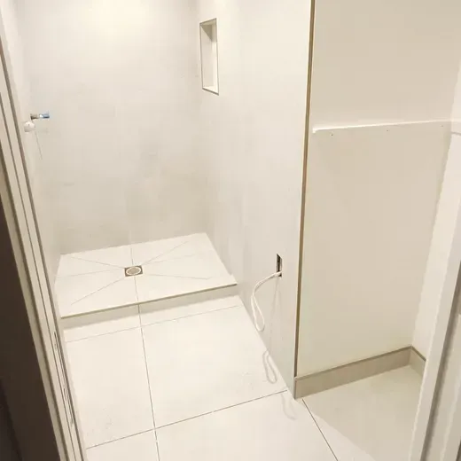 Small white tiled bathroom with a low step and a grab cord on the wall