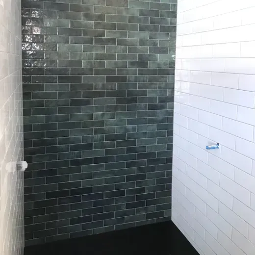 Empty tiled shower with dark gray back wall and white side wall, black floor, and a blue fixture on the right