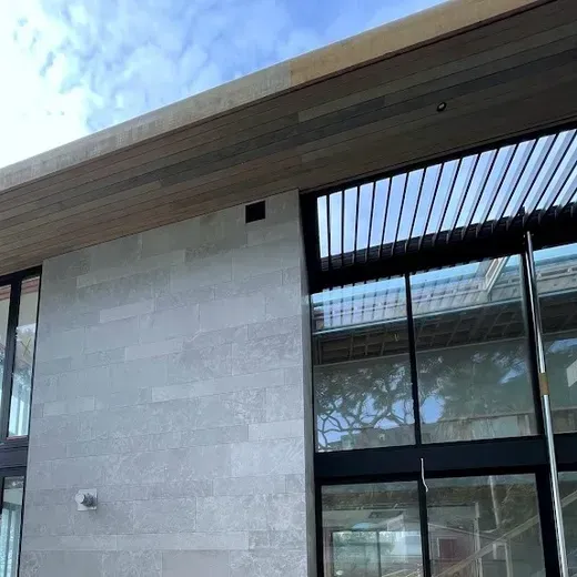 Modern building exterior with light stone walls, wood roof trim, and large glass windows
