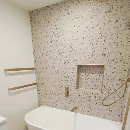 Small bathroom with white tub, speckled tile wall, grab bars, and a built-in shower niche.