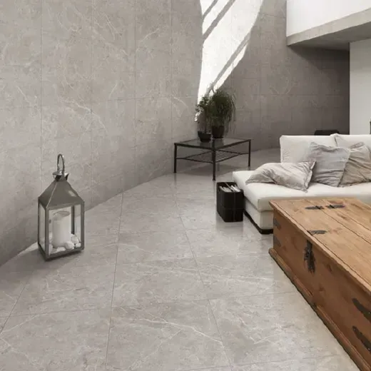 Minimalist living room with gray tiled floor, beige sofa, wooden chest, lantern, and potted plant near a skylight