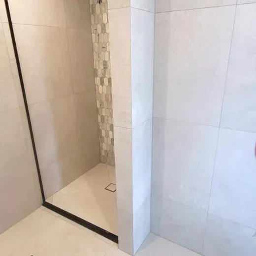Modern shower stall with beige and white tiled walls and a glass partition