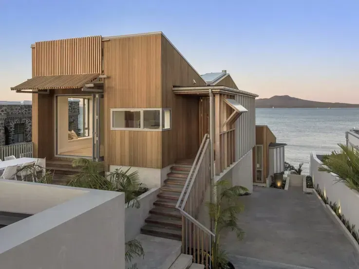 Modern wooden house with stairs overlooking the water at sunset