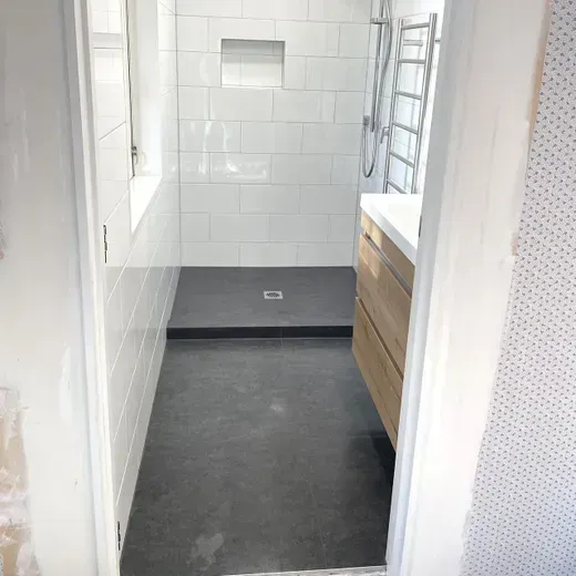 Small modern bathroom with white tiled walls, black floor, sink vanity, and ladder towel rack