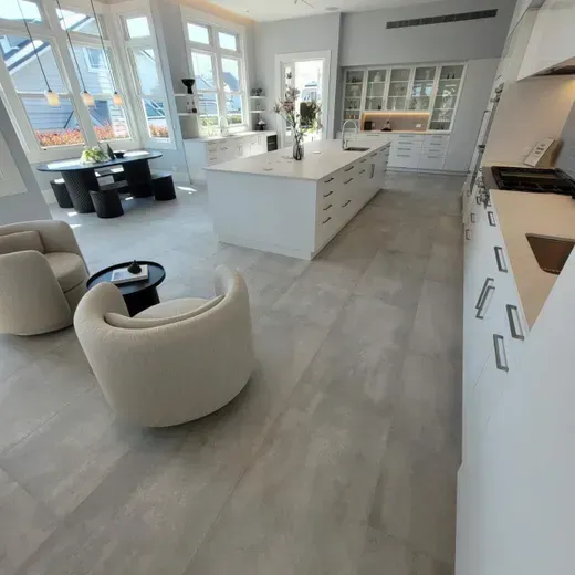 Bright modern kitchen with white cabinets, large island, and lounge chairs by sunlit windows