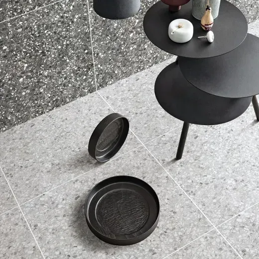Black round side table with detached tray on speckled gray floor, holding a small candle and decor pieces