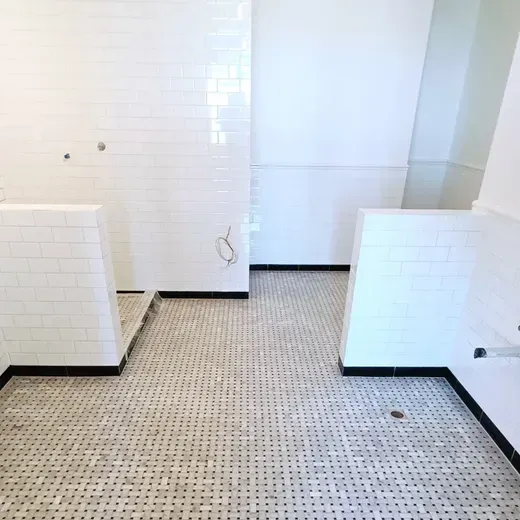 Empty tiled bathroom with white walls and black trim, showing a shower area and floor drain.