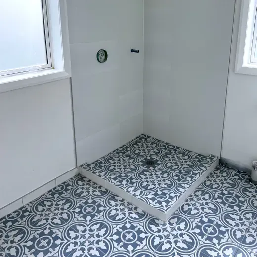 Small tiled bathroom corner with blue-and-white patterned floor and a shower base under windows.