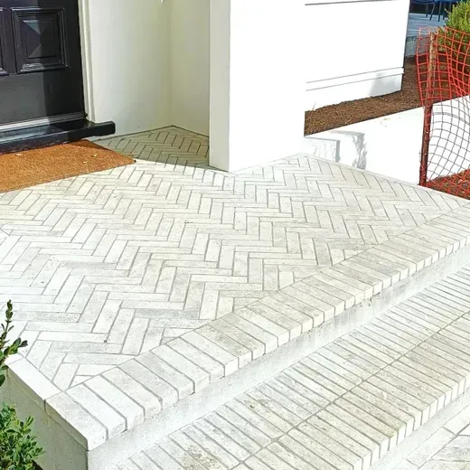 White herringbone-tile front steps and porch beside a black door and white wall