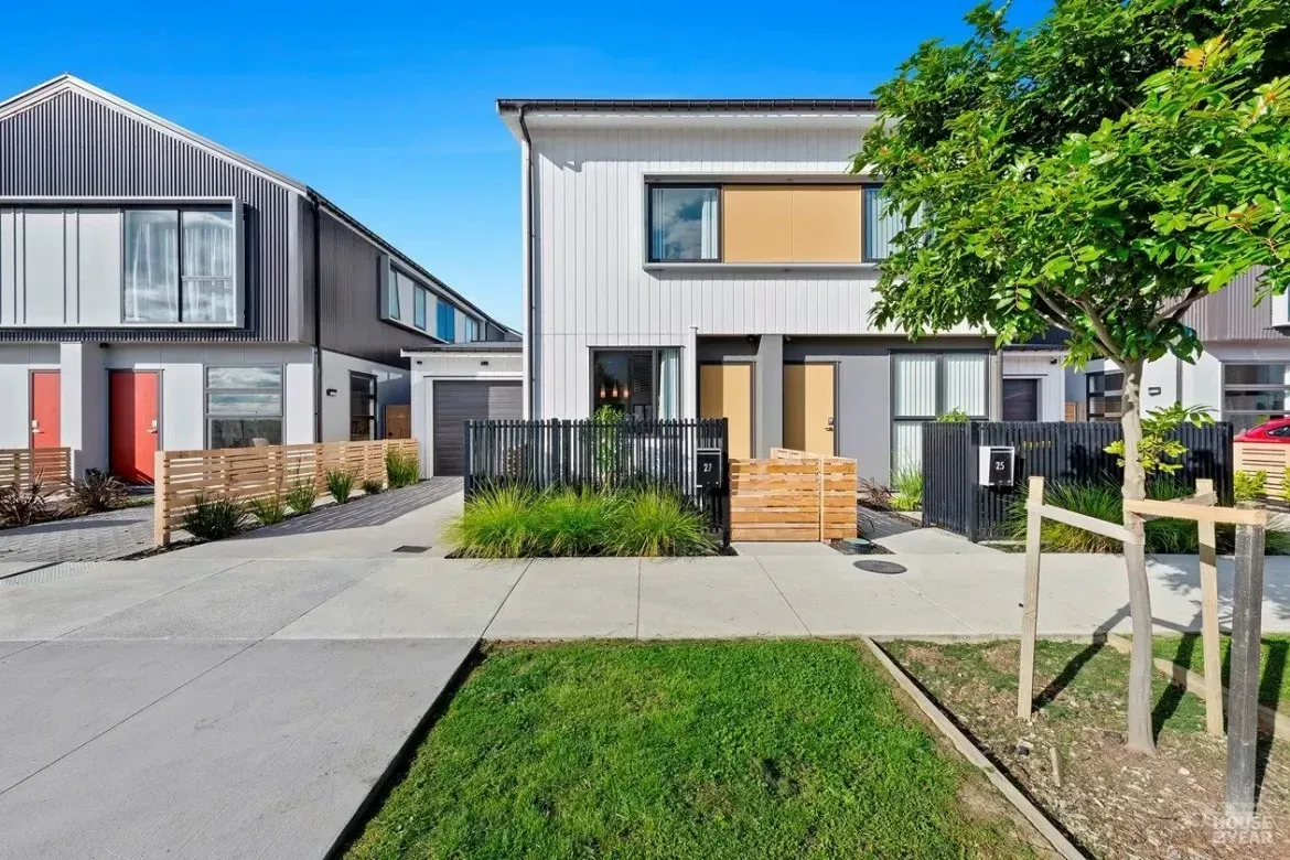 Modern suburban townhouses with front yards, driveways, and a tree-lined street under a blue sky