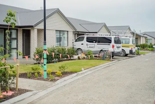 Suburban street with modern homes, a white van, and a landscaped front yard under overcast skies