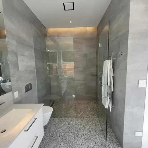Modern gray-tiled bathroom with walk-in glass shower and white vanity sink.