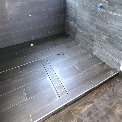 Empty tiled shower with gray walls, floor drain, and bench seat
