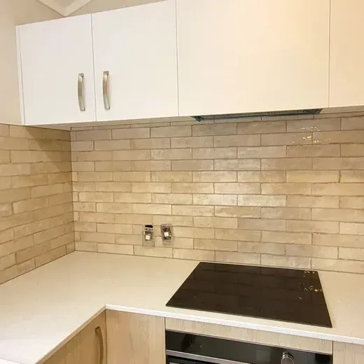 Compact kitchen corner with white cabinets, beige tile backsplash, and black cooktop.