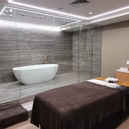 Modern spa room with a massage table, freestanding tub, and glass-walled bathroom