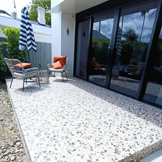 Modern patio with terrazzo floor, black sliding doors, and orange chairs beside a striped umbrella