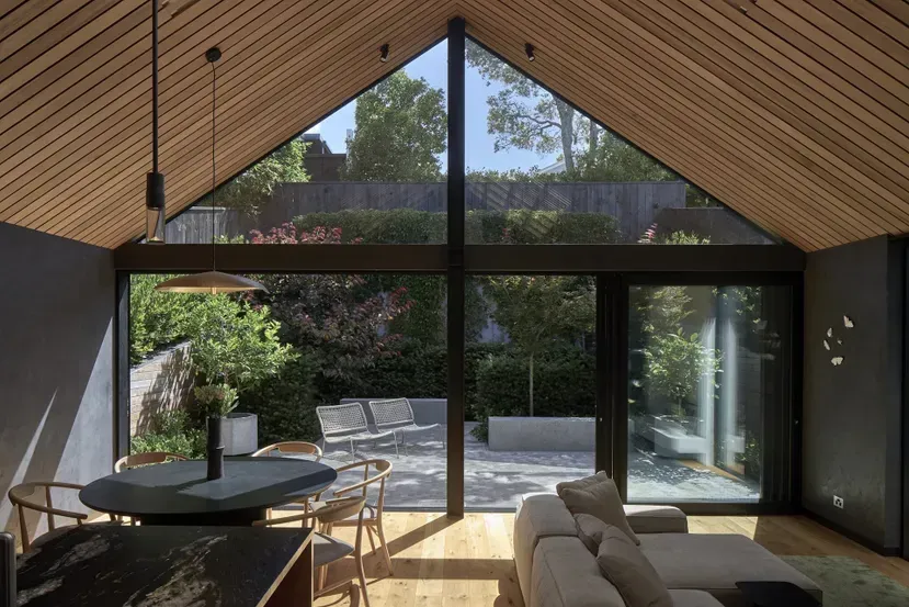 Modern living room with vaulted wood ceiling and floor-to-ceiling glass doors overlooking a patio and greenery