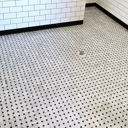White tiled bathroom floor and walls with a floor drain and black trim.