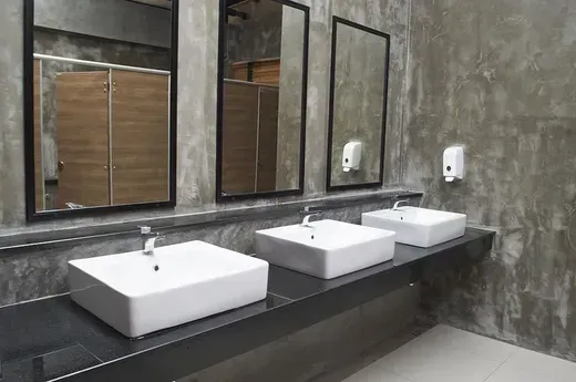 Modern bathroom with three white sinks, mirrors, and gray concrete walls
