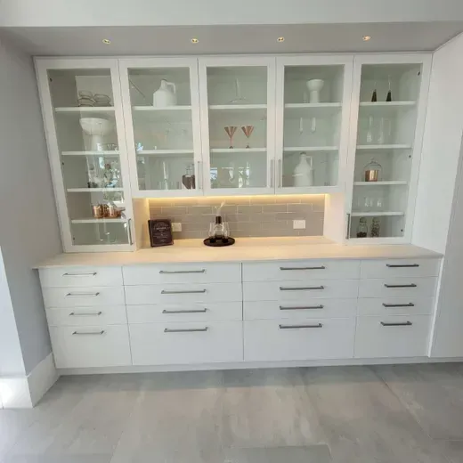 White built-in cabinet with glass display shelves, drawers, and warm backlit countertop in a modern room