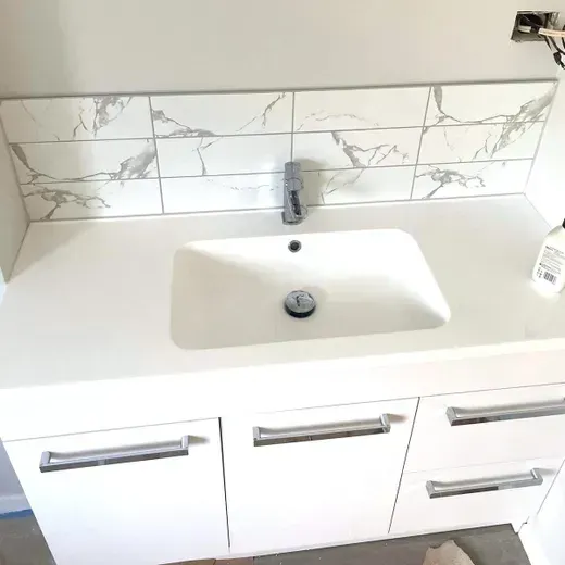 Modern bathroom sink with white vanity, chrome faucet, marble-look backsplash, and three drawers
