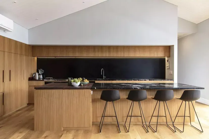 Modern wood kitchen with black island, bar stools, and a black backsplash under a vaulted ceiling
