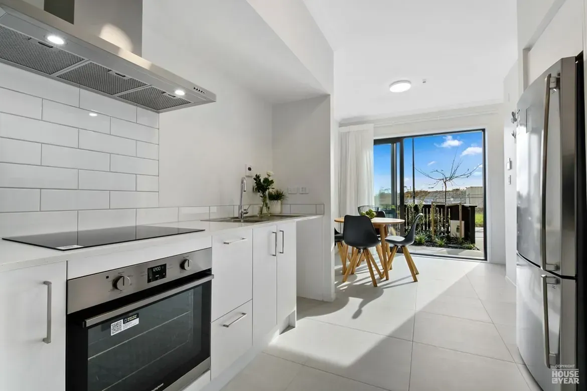 Bright modern white kitchen opening to a sunlit balcony with a small dining table and city view